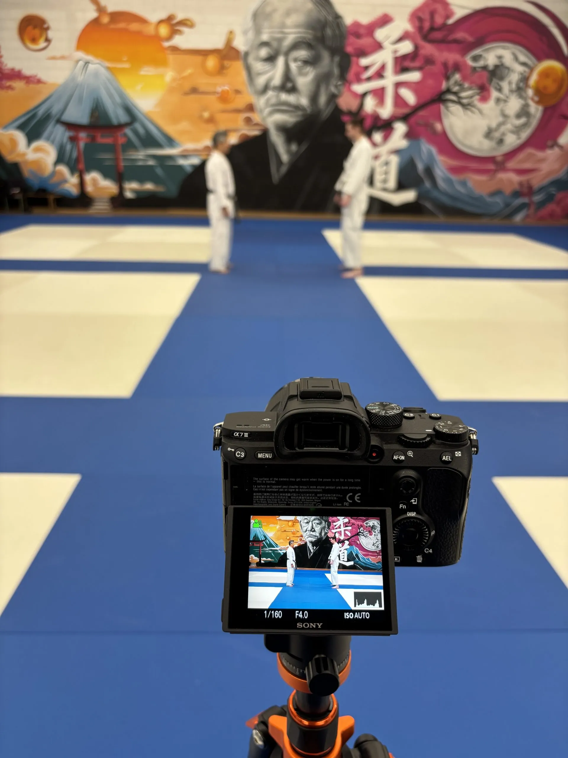 Caméra Sony sur trépied face à deux judokas dans un dojo décoré d’une fresque